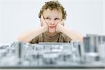 Little boy sitting with computer motherboard, holding head, looking away