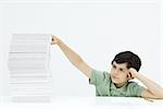 Boy sitting with tall stack of papers, holding head, frowning