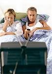Couple lying in bed watching television.