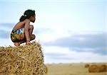 Girl crouching on haystack, side view