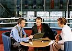 Two men and a woman sitting at table, looking at laptop computer