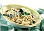 Fettuccini with fresh basil and black olives in bowl, on green and white checked tablecloth, close-up