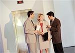 Two businessmen and a businesswoman standing in front of elevator