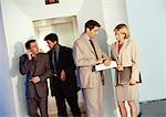 Business associates in front of elevator, man looking down at his watch