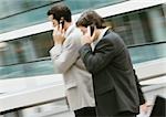 Two businessmen using cell phones outside, side view