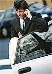 Businessman using cell phone, elbow on car door
