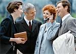 Four business people standing outside smiling, businesswoman on cell phone