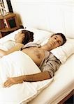 Couple lying in bed with heads turned in opposite directions