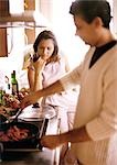 Man cooking in blurred foreground, woman holding glass in background