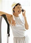 Woman talking on phone, leaning elbow on vacuum cleaner, waist up