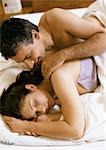 Couple lying in bed, man touching woman's shoulder