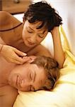 Couple lying in bed, woman stroking man's cheek