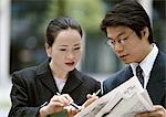 Businessman, businesswoman together looking at newspaper