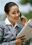 Businesswoman using cell phone, holding newspaper, portrait