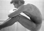 Nude man sitting, leaning on knees, side view, b&w