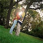 Young man and woman standing on grass, embracing, side view, full length