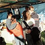 Young couples with arms around each other, standing in street market, rear view