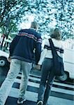 Young couple holding hands, crossing at pedestrian crossing, blurred, rear view