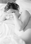 Femme nue allongée sur le lit, toucher le visage avec l'arrière de la main, noir et blanc