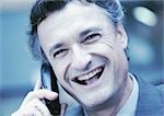 Businessman using cellular phone, laughing, close-up, cool toned.