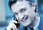 Businessman using cellular phone, smiling at camera, close-up, cool toned.