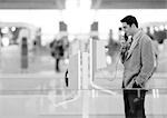 Businessman using pay phone in terminal, black and white.