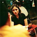 Young woman sitting at table and smoking, second person blurred in foreground