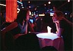 Young man and woman sitting in bar, talking at table, dramatic lighting.