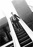 Businessman going down escalator, b&w.