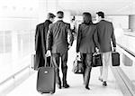 Group of business people walking through terminal, full length, rear view, b&w.