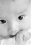 Baby's face with hand in mouth, close-up, B&W.