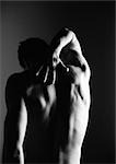 Nude man touching back, rear view, black and white, silhouette.