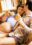 Man on sofa kissing pregnant woman, both holding croissants