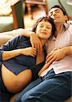 Pregnant woman and man lying on sofa, smiling