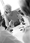 Mature businesswoman in conference, using cell phone, other businesspeople blurred in foreground, B&W