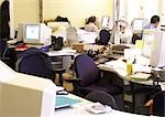 Desks and computers in office, people working in background