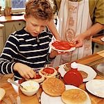 Enfant garnir les hamburgers, les adultes tenant assiette de tranches de tomate
