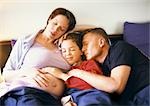 Pregnant woman sitting with man and child in bed