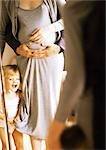 Pregnant woman and child in front of mirror, man's arms around woman's stomach