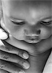 Baby with adult hand on chest, close-up, b&w