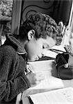 Boy sitting at desk, writing in notebook, side view, b&w