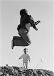 Boy jumping and little girl walking in background, low angle view, b&w