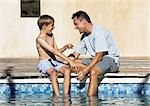 Man and young boy sitting together, feet in pool.