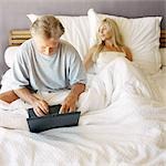 Couple in bed, man using laptop