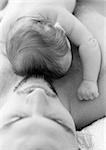 Father lying down with infant on chest, high angle view, b&w