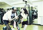 Woman standing next to man using exercise equipment in gym, laughing