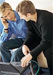 Deux jeunes hommes, l'un à l'aide d'ordinateur portable, à l'aide d'un téléphone cellulaire.