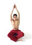 Topless homme assis sur un style indien floor, méditant les bras vers le haut sur la tête