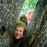 Two mature men and a woman looking at camera from between trees