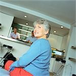 Mature woman sitting, looking over shoulder, men standing in kitchen in background